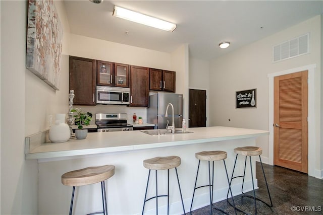 1020 Porter St Unit 103, Richmond, VA 23224 - kitchen featuring appliances with stainless steel finishes, a sink, dark brown cabinets, a kitchen bar, and light countertops