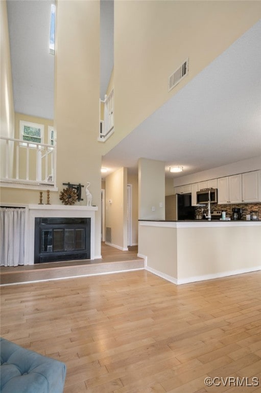 2615 Towngate Ct, Henrico, VA 23233 - unfurnished living room featuring a high ceiling, light wood-style flooring, a glass covered fireplace, and baseboards