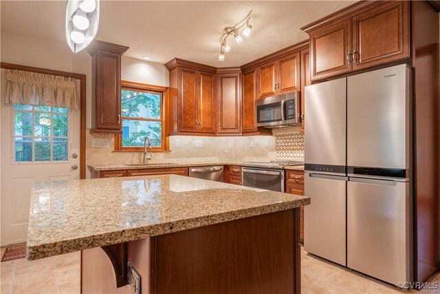 13100 Spring Trace Pl, Midlothian, VA 23112 - kitchen featuring appliances with stainless steel finishes, light stone counters, brown cabinetry, tasteful backsplash, and a kitchen island