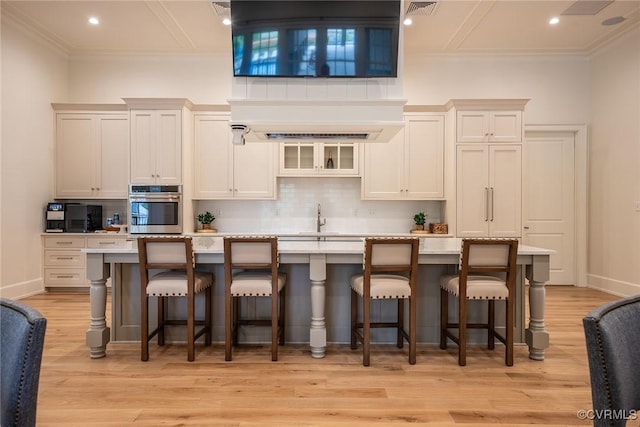 9008 Mirage Mews, Richmond, VA 23238 - kitchen with oven, ornamental molding, decorative backsplash, light wood-type flooring, and a center island with sink