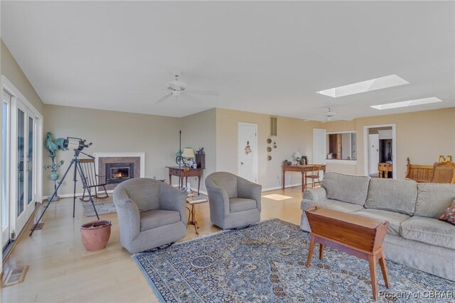 159 Fleeton Point Cir, Reedville, VA 22539 - living room featuring a skylight, wood finished floors, a ceiling fan, a warm lit fireplace, and baseboards