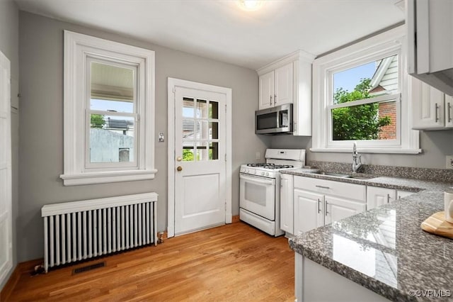 3204 Griffin Ave, Richmond, VA 23222 - kitchen with radiator heating unit, white range with gas cooktop, stainless steel microwave, a sink, and light wood-style flooring