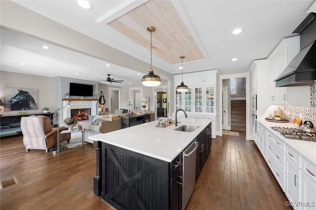 3397 Manor Oaks Dr, Powhatan, VA 23139 - kitchen featuring stainless steel appliances, wall chimney exhaust hood, light countertops, a warm lit fireplace, and white cabinetry