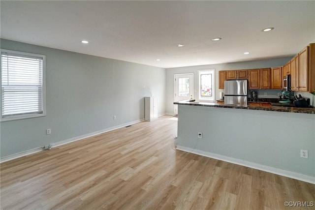 3107 Q St, Richmond, VA 23223 - kitchen featuring appliances with stainless steel finishes, brown cabinetry, light wood-style floors, a peninsula, and dark stone counters