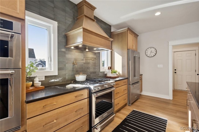 9463 Angels Share Dr, New Kent, VA 23124 - kitchen with custom exhaust hood, stainless steel appliances, decorative backsplash, light wood finished floors, and baseboards