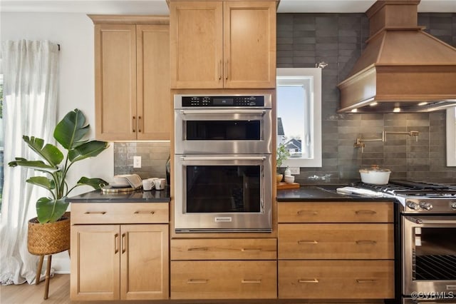 9463 Angels Share Dr, New Kent, VA 23124 - kitchen with appliances with stainless steel finishes, custom exhaust hood, dark countertops, backsplash, and light brown cabinetry