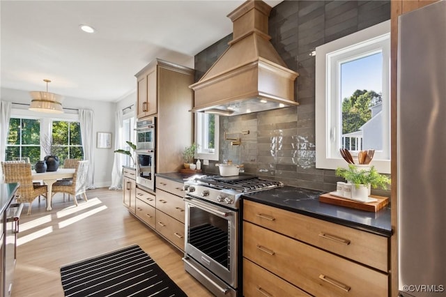 9463 Angels Share Dr, New Kent, VA 23124 - kitchen with custom exhaust hood, stainless steel appliances, dark countertops, decorative backsplash, and light wood-style flooring