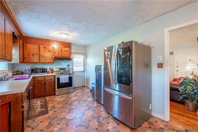 18517 Depot Rd, Mc Kenney, VA 23872 - kitchen with appliances with stainless steel finishes, brown cabinetry, light countertops, under cabinet range hood, and a textured ceiling