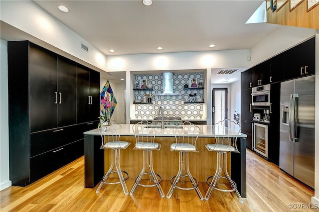 26171/2 Floyd Ave, Richmond, VA 23220 - kitchen with stainless steel refrigerator with ice dispenser, dark cabinetry, a kitchen bar, light wood-style floors, and a center island with sink