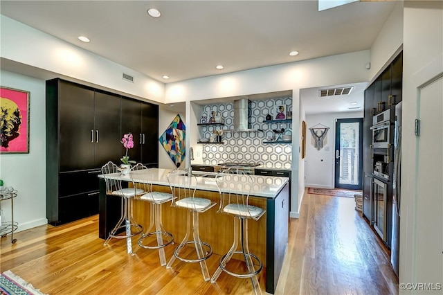 26171/2 Floyd Ave, Richmond, VA 23220 - kitchen with light wood-style flooring, light countertops, a kitchen breakfast bar, wall chimney exhaust hood, and recessed lighting