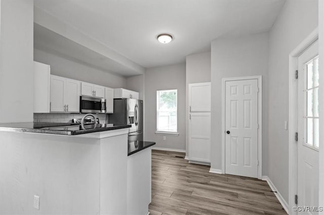 1317 N 22nd St, Richmond, VA 23223 - kitchen with appliances with stainless steel finishes, white cabinets, backsplash, wood finished floors, and a peninsula