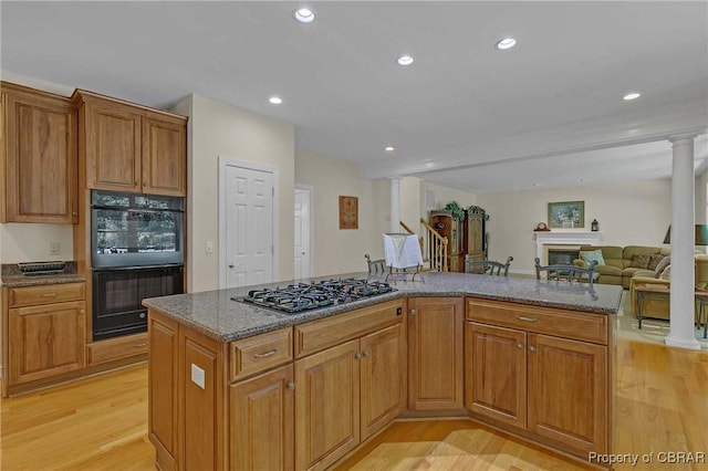 1708 Centennial Dr, Toano, VA 23168 - kitchen with stainless steel gas cooktop, decorative columns, light wood-style floors, dark stone counters, and a kitchen island