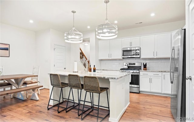 18304 Palisades Ct, Moseley, VA 23120 - kitchen with appliances with stainless steel finishes, a kitchen island with sink, decorative backsplash, light wood-style floors, and a breakfast bar