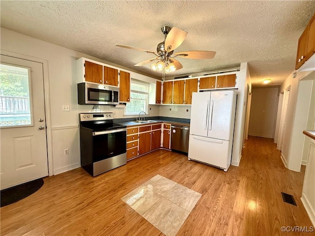 241 Levelfield Ln, Lancaster, VA 22503 - kitchen with appliances with stainless steel finishes, a sink, brown cabinets, light wood finished floors, and a textured ceiling