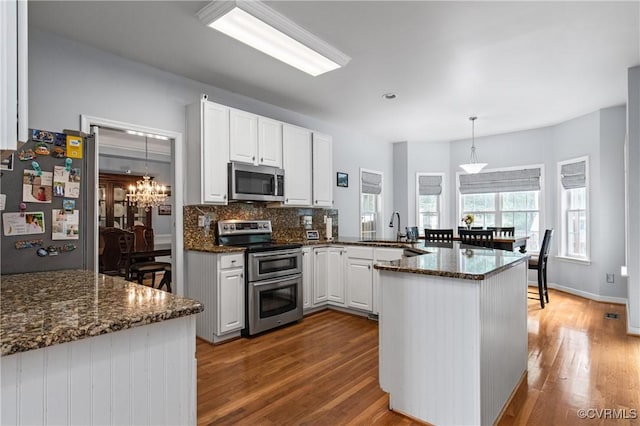 8940 Kings Charter Dr, Hanover, VA 23116 - kitchen featuring stainless steel appliances, a peninsula, wood finished floors, a chandelier, and white cabinets