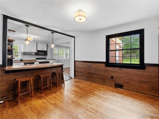 8525 Mark Lawn Dr, Henrico, VA 23229 - kitchen featuring black microwave, light wood finished floors, a kitchen bar, white stove, and pendant lighting