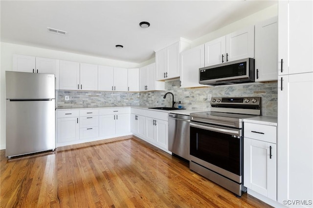 1312 St Michaels Ln, Richmond, VA 23229 - kitchen featuring stainless steel appliances, light countertops, tasteful backsplash, white cabinets, and light wood-type flooring