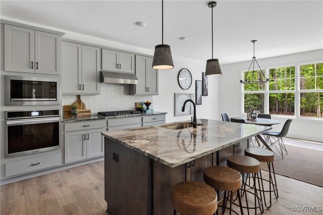 9496 Angels Share Dr, New Kent, VA 23124 - kitchen with stainless steel appliances, a sink, light wood-style floors, stone countertops, and under cabinet range hood