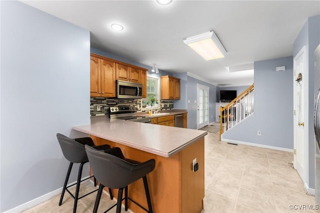 15619 Winding Ash Dr, Chesterfield, VA 23832 - kitchen featuring stainless steel appliances, brown cabinetry, a peninsula, a kitchen bar, and tasteful backsplash