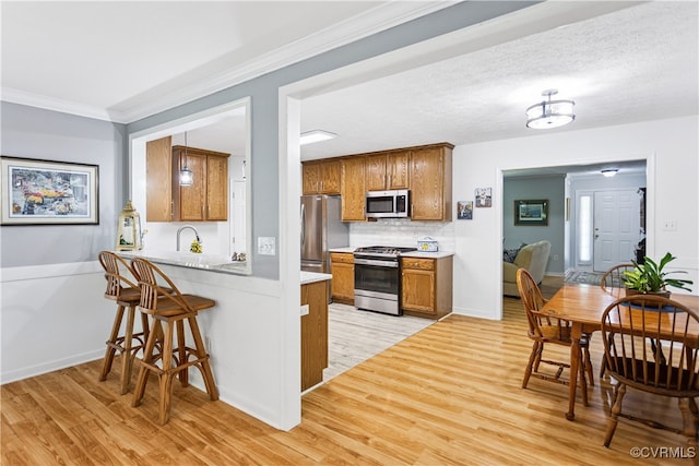 3826 Minitree Glen Dr, Providence Forge, VA 23140 - kitchen featuring stainless steel appliances, light wood-style floors, a peninsula, brown cabinets, and crown molding