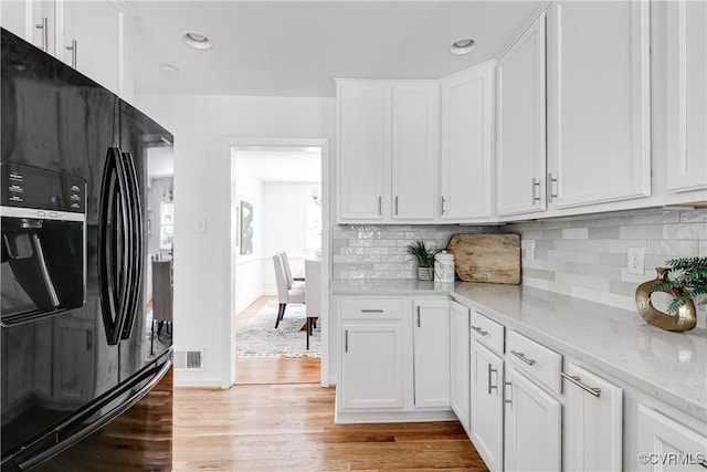 7654 Cherokee Rd, Richmond, VA 23225 - kitchen with black fridge, light wood-style flooring, white cabinets, light stone counters, and tasteful backsplash