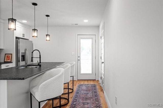1508 N 29th St, Richmond, VA 23223 - kitchen with stainless steel fridge with ice dispenser, dark countertops, light wood-style floors, a kitchen bar, and white cabinetry