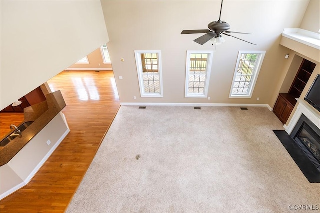 706 Colony Oak Ln, Midlothian, VA 23114 - unfurnished living room with a fireplace with flush hearth, plenty of natural light, a ceiling fan, light wood-style flooring, and a high ceiling