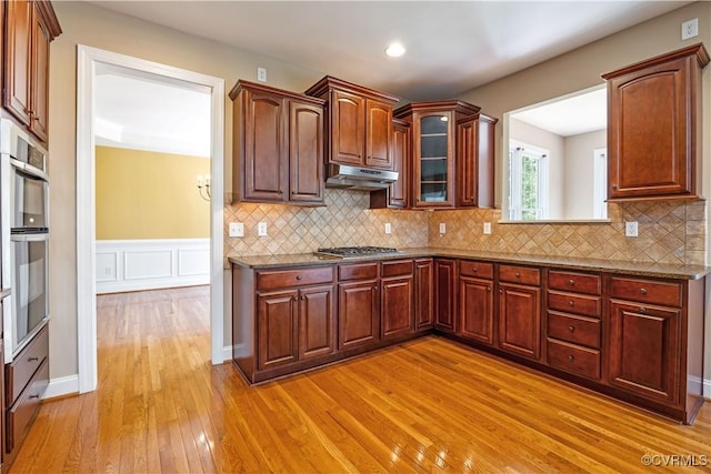 706 Colony Oak Ln, Midlothian, VA 23114 - kitchen featuring light wood-style flooring, under cabinet range hood, decorative backsplash, glass insert cabinets, and stainless steel gas stovetop