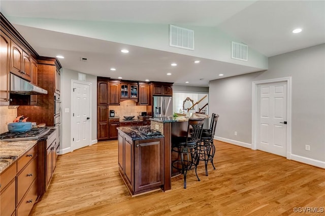 9065 Greenlake Cir, Mechanicsville, VA 23116 - kitchen featuring under cabinet range hood, stainless steel appliances, a kitchen breakfast bar, tasteful backsplash, and light wood-type flooring