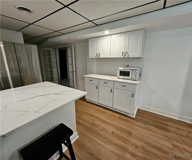 10278 Henderson Hall Rd, Mechanicsville, VA 20116 - kitchen with white microwave, a paneled ceiling, light wood-style floors, light stone counters, and white cabinets