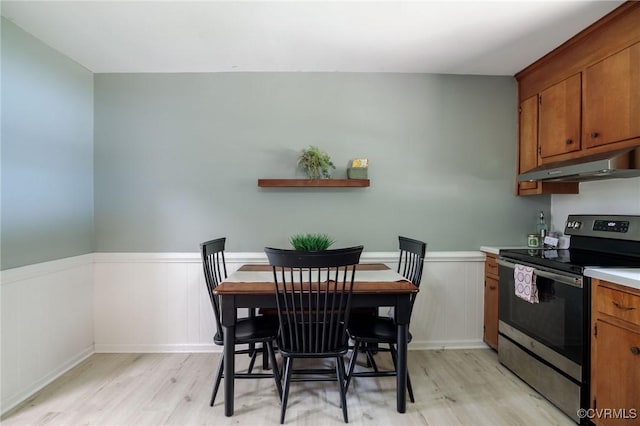 2000 Point Of Rocks Rd, Chester, VA 23836 - kitchen featuring stainless steel range with electric stovetop, under cabinet range hood, light wood finished floors, brown cabinets, and a wainscoted wall