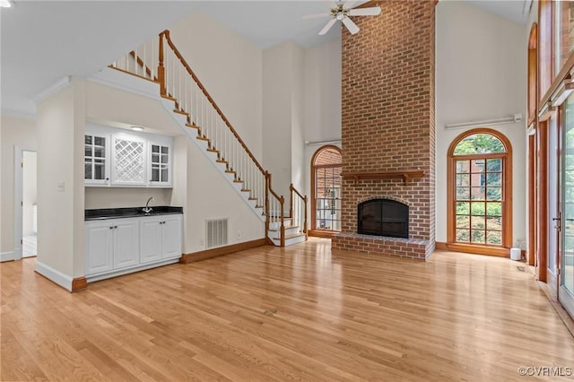 9261 Royal Grant Dr, Hanover, VA 23116 - unfurnished living room with a towering ceiling, light wood-style floors, stairs, a brick fireplace, and ceiling fan