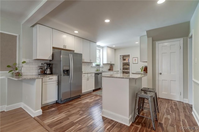 4824 Coleman Rd, Richmond, VA 23230 - kitchen with appliances with stainless steel finishes, wood finished floors, white cabinets, backsplash, and a breakfast bar