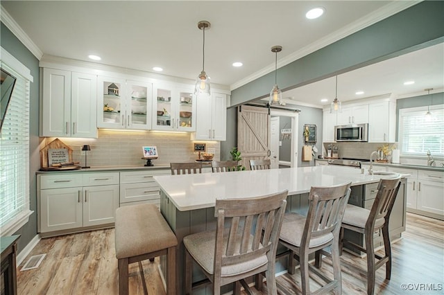 1442 Dorset Rd, Powhatan, VA 23139 - kitchen with a barn door, light wood-style floors, backsplash, stainless steel microwave, and white cabinetry
