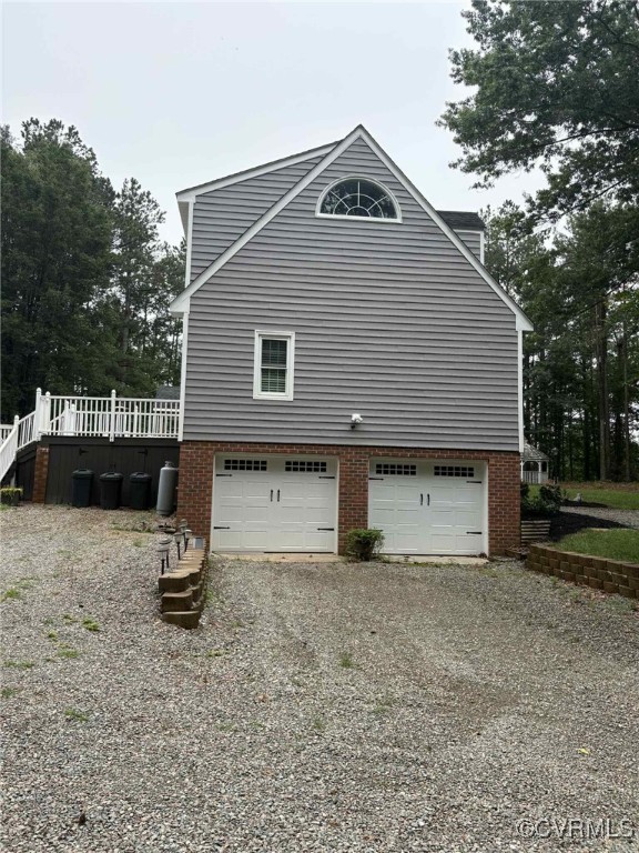 1442 Dorset Rd, Powhatan, VA 23139 - view of home's exterior with gravel driveway, a garage, brick siding, stairway, and a wooden deck