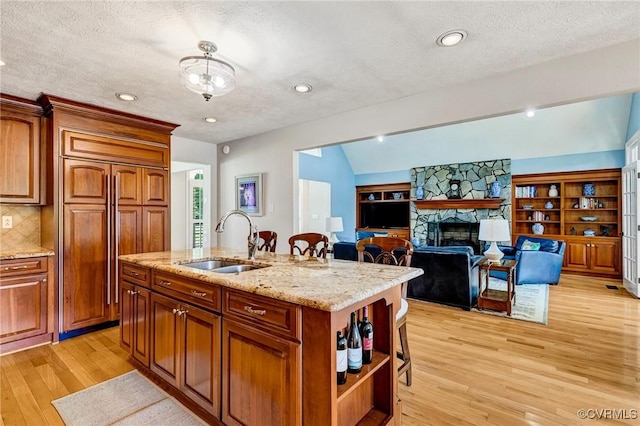 8467 Wendellshire Way, Mechanicsville, VA 23111 - kitchen with light wood-style floors, open shelves, an island with sink, a stone fireplace, and a textured ceiling