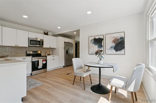 808 Penniman Rd, Williamsburg, VA 23185 - kitchen with appliances with stainless steel finishes, decorative backsplash, white cabinetry, light countertops, and light wood-style flooring