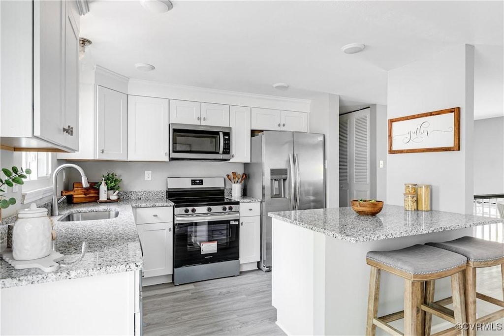 2200 Old Indian Rd, Richmond, VA 23235 - kitchen featuring stainless steel appliances, white cabinets, light stone countertops, a kitchen breakfast bar, and light wood finished floors