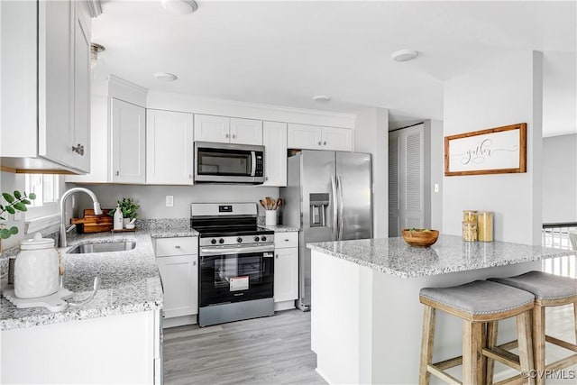 2200 Old Indian Rd, Richmond, VA 23235 - kitchen featuring stainless steel appliances, white cabinets, light stone countertops, a kitchen breakfast bar, and light wood finished floors
