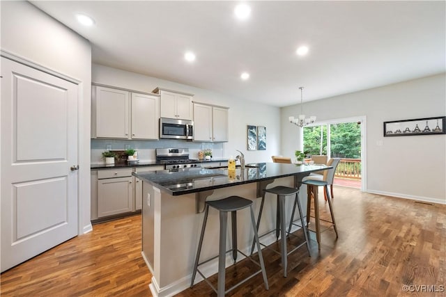 15037 Hazelbury Cir, Midlothian, VA 23112 - kitchen with stainless steel appliances, light wood finished floors, a breakfast bar area, gray cabinets, and a kitchen island with sink
