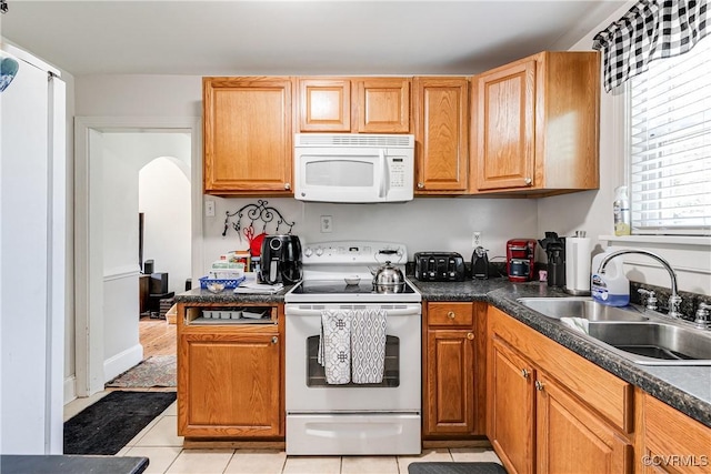 18 E 36th St, Richmond, VA 23224 - kitchen with white appliances, light tile patterned flooring, arched walkways, dark countertops, and brown cabinets