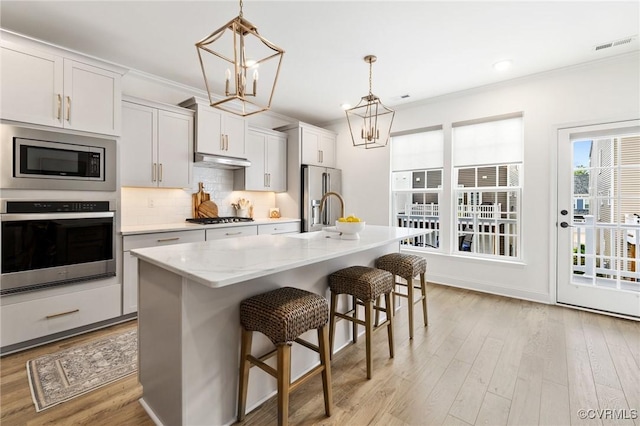 6988 Leire Ln, Chesterfield, VA 23832 - kitchen featuring appliances with stainless steel finishes, a chandelier, light wood-style floors, a breakfast bar area, and tasteful backsplash