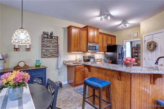 5669 Virginia Park Dr, Providence Forge, VA 23140 - kitchen featuring stainless steel appliances, a kitchen breakfast bar, brown cabinetry, light stone countertops, and hanging light fixtures