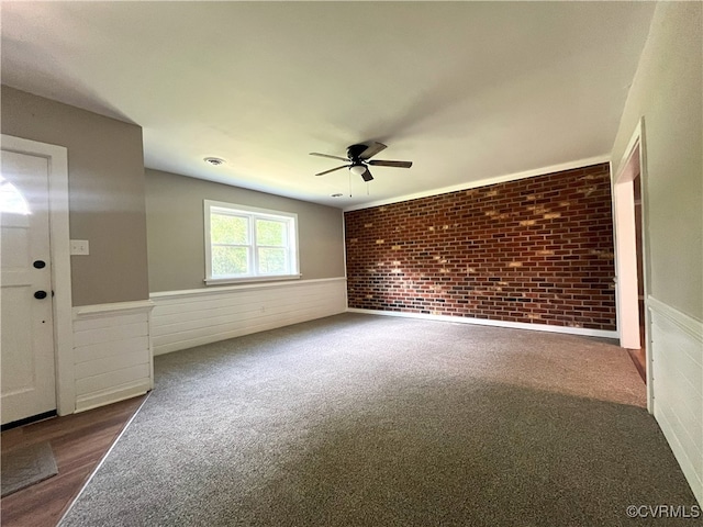 12027 Old Buckingham Rd, Midlothian, VA 23113 - empty room featuring ceiling fan, a wainscoted wall, brick wall, and dark carpet