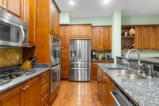 9522 Nassington Ct, Henrico, VA 23229 - kitchen with stainless steel appliances, brown cabinetry, dark stone counters, light wood finished floors, and hanging light fixtures
