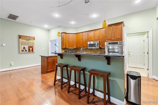 9522 Nassington Ct, Henrico, VA 23229 - kitchen featuring stainless steel appliances, light wood finished floors, a breakfast bar, brown cabinetry, and tasteful backsplash