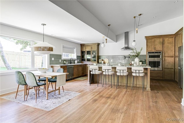 7418 Cherokee Rd, Richmond, VA 23225 - kitchen with appliances with stainless steel finishes, wall chimney exhaust hood, light countertops, a kitchen island with sink, and light wood-style floors