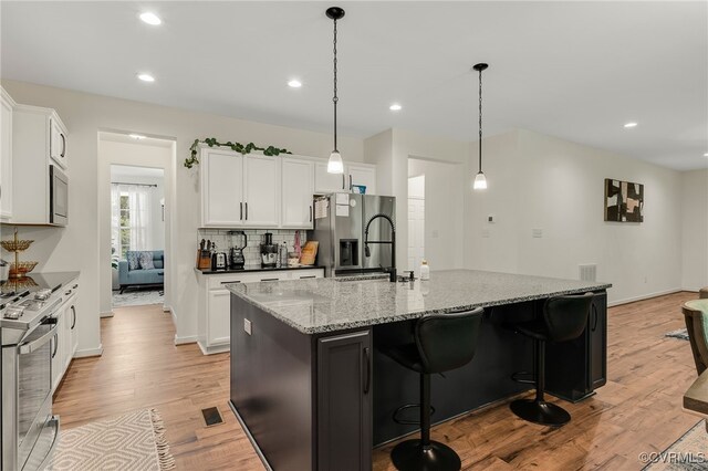 6112 Water Violet Ter, Moseley, VA 23120 - kitchen with stainless steel appliances, light wood-style floors, white cabinets, light stone countertops, and a kitchen breakfast bar