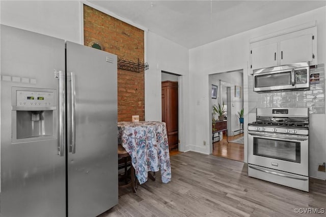 306 Hamilton Ave, Colonial Heights, VA 23834 - kitchen featuring stainless steel appliances, light wood-style flooring, white cabinetry, tasteful backsplash, and brick wall