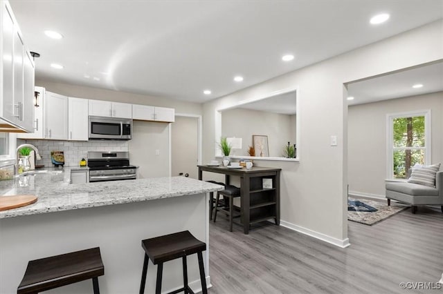 2718 Colgrave Rd, Chesterfield, VA 23112 - kitchen with appliances with stainless steel finishes, a peninsula, light wood-style floors, white cabinetry, and tasteful backsplash